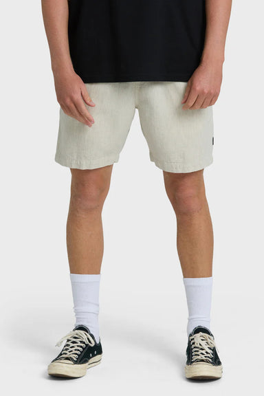 Man wearing beige shorts, black shirt, white socks, and black sneakers on a white background