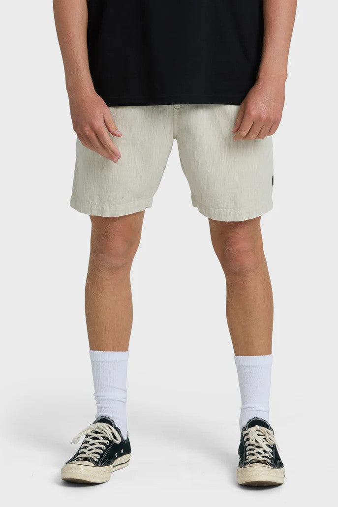 Man wearing beige shorts, black shirt, white socks, and black sneakers on a white background