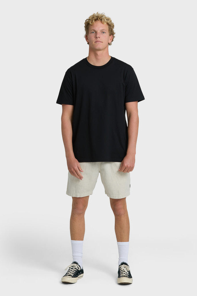 Man wearing beige shorts, black shirt, white socks, and black sneakers on a white background