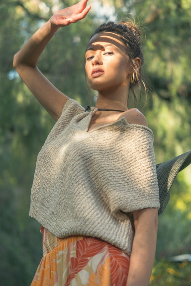 Woman wearing a beige knitted top and colorful skirt outdoors with greenery in the background