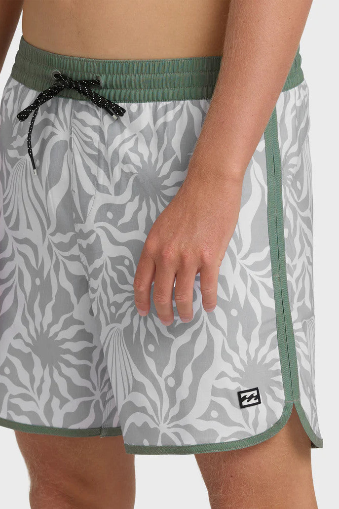 Man wearing gray swim trunks with a leaf pattern and contrasting green elastic waistband with drawstring on a white background