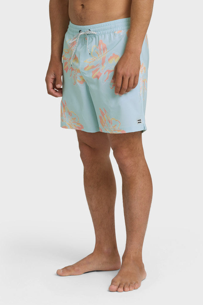 Man wearing light blue swim trunks with a yellow and orange oversized floral pattern and elastic waistband with drawstring on a white background