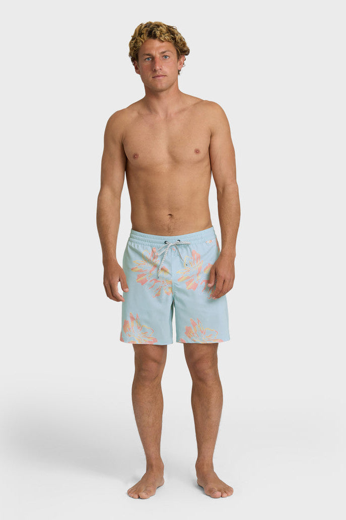 Man wearing light blue swim trunks with a yellow and orange oversized floral pattern and elastic waistband with drawstring on a white background