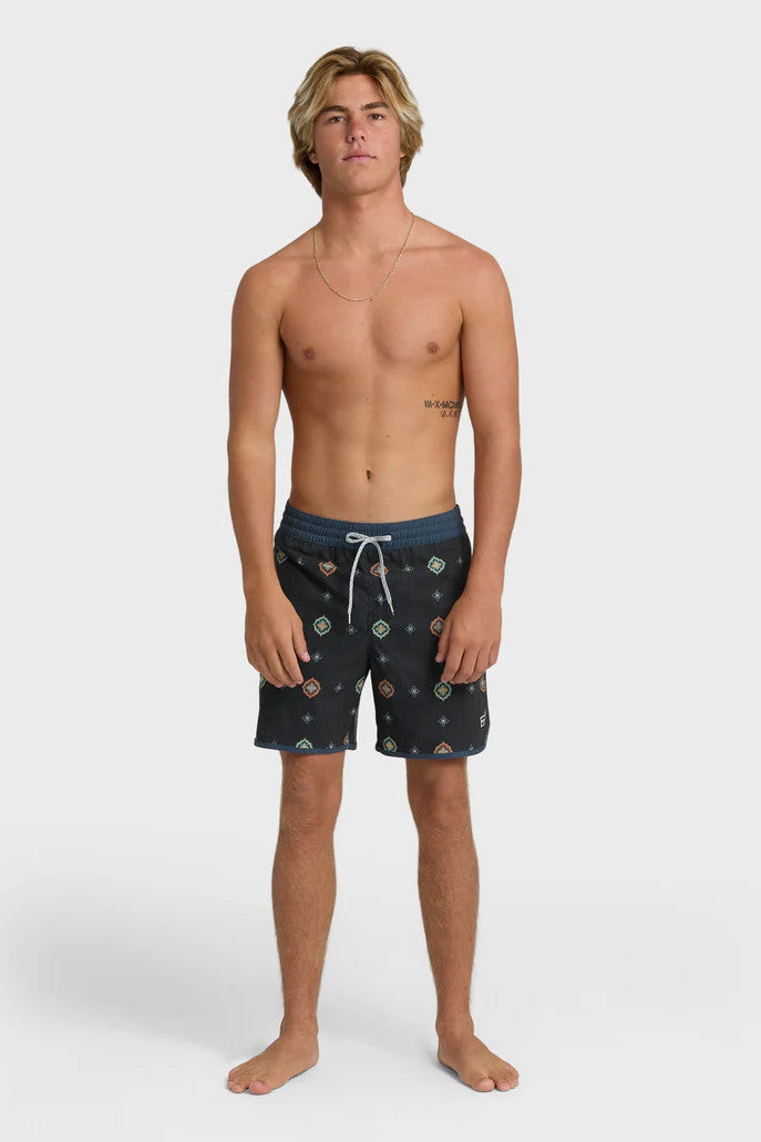 Man wearing charcoal swim trunks with a light blue and orange pattern pattern and contrasting navy elastic waistband with drawstring on a white background