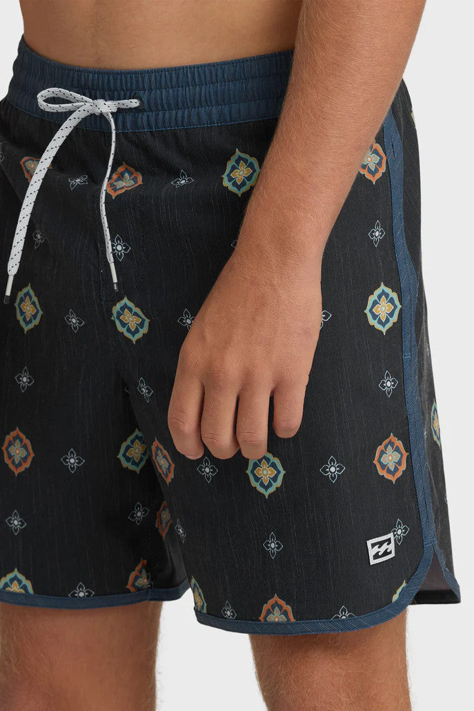 Man wearing charcoal swim trunks with a light blue and orange pattern pattern and contrasting navy elastic waistband with drawstring on a white background