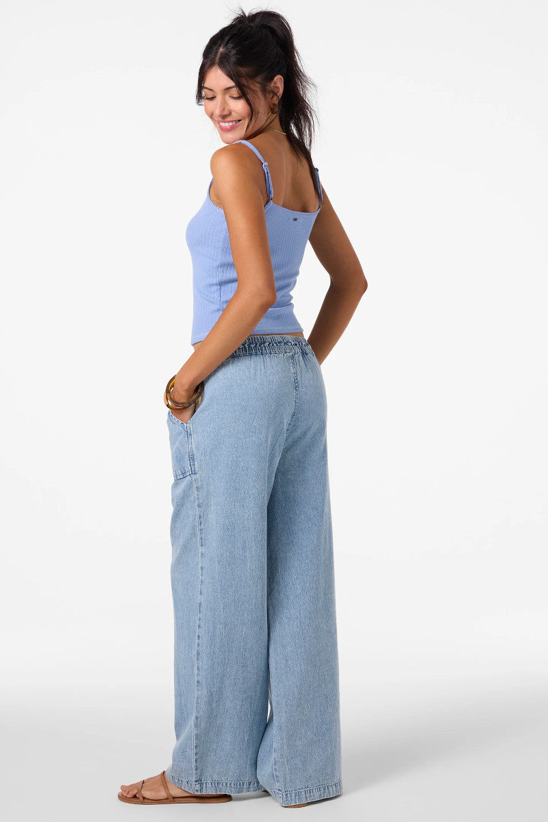 Woman wearing a light blue tank top and wide-leg jeans on a white background