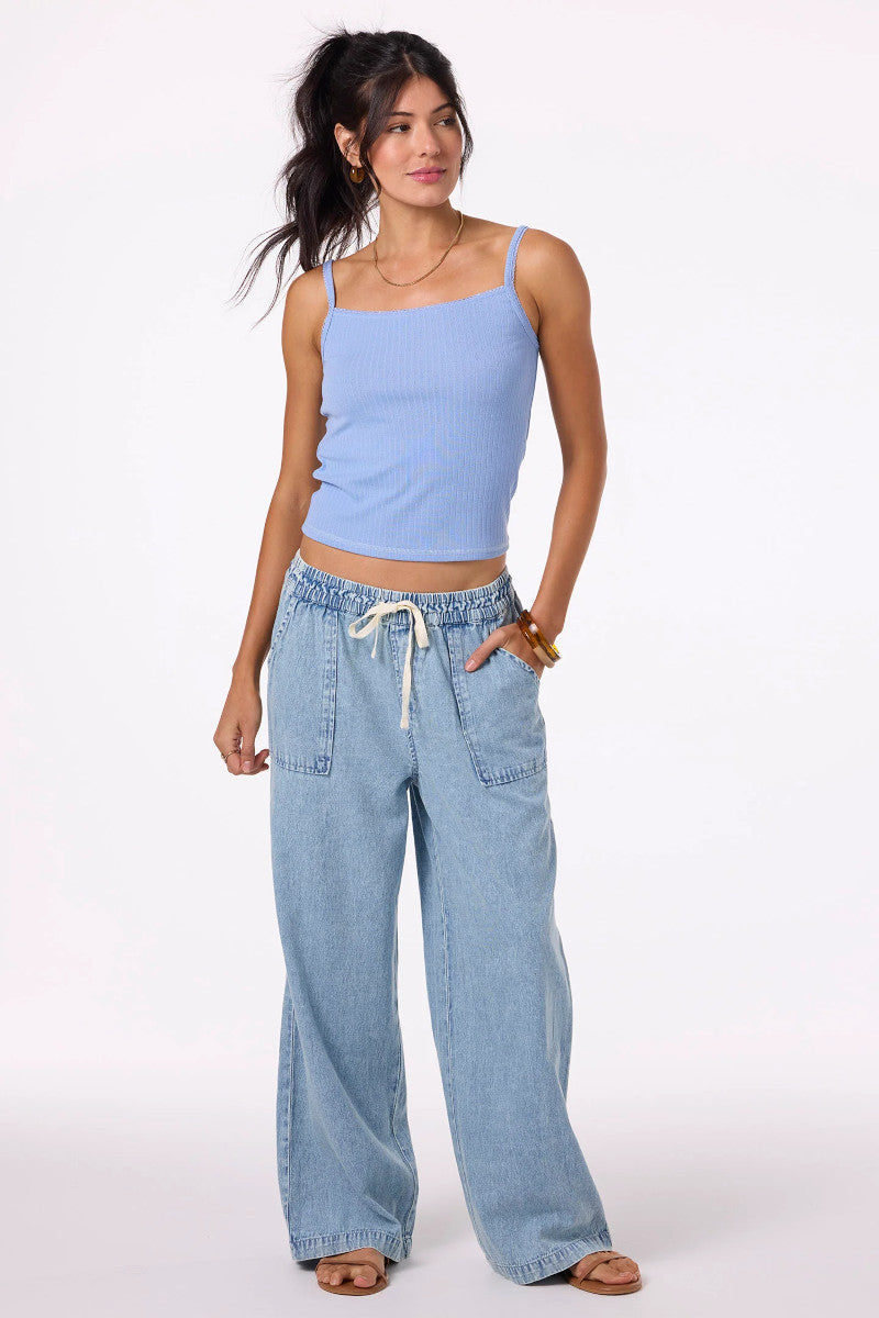 Woman wearing a light blue tank top and wide-leg jeans on a white background