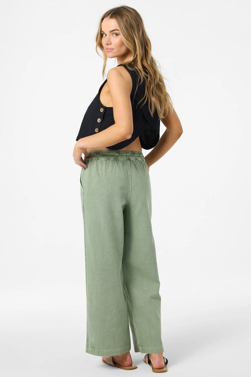 Woman wearing a black sleeveless top with button details and green wide-leg pants on a white background