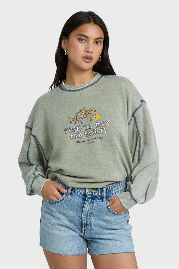 Woman wearing a gray-green sweatshirt with a graphic design and blue shorts on a white background