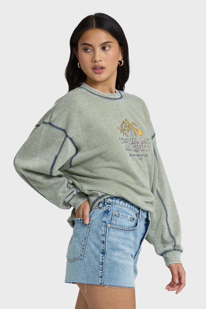 Woman wearing a gray-green sweatshirt with a graphic design and blue shorts on a white background