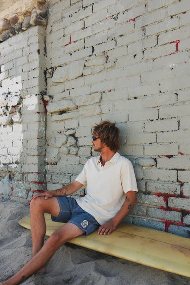 Man sitting on a wooden bench against a textured wall.