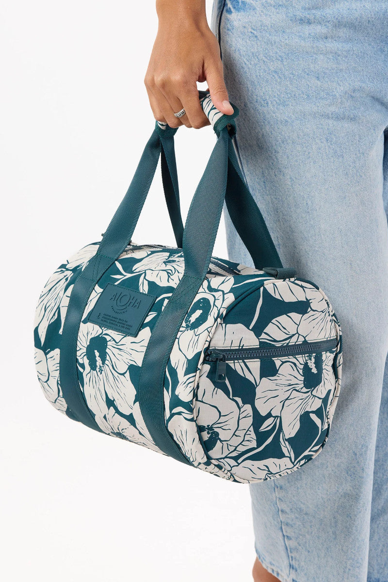 Person holding a floral patterned duffel bag with blue straps against a white background