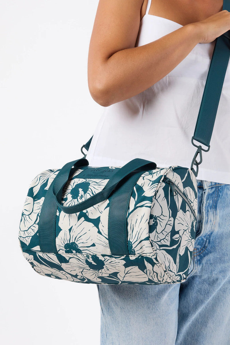 Person holding a floral duffel bag with dark teal straps on a white background