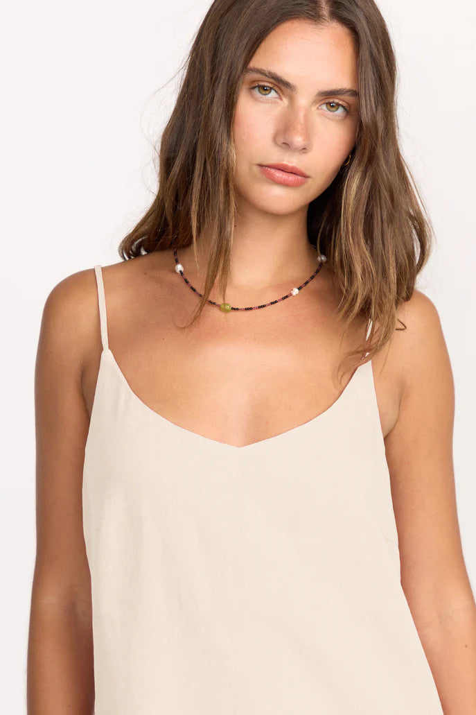 Woman wearing a beige spaghetti strap top against a white background