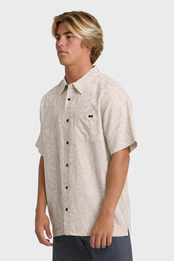 Man wearing a pink-grey short-sleeve button-up shirt with a tonal leaf pattern on a white background