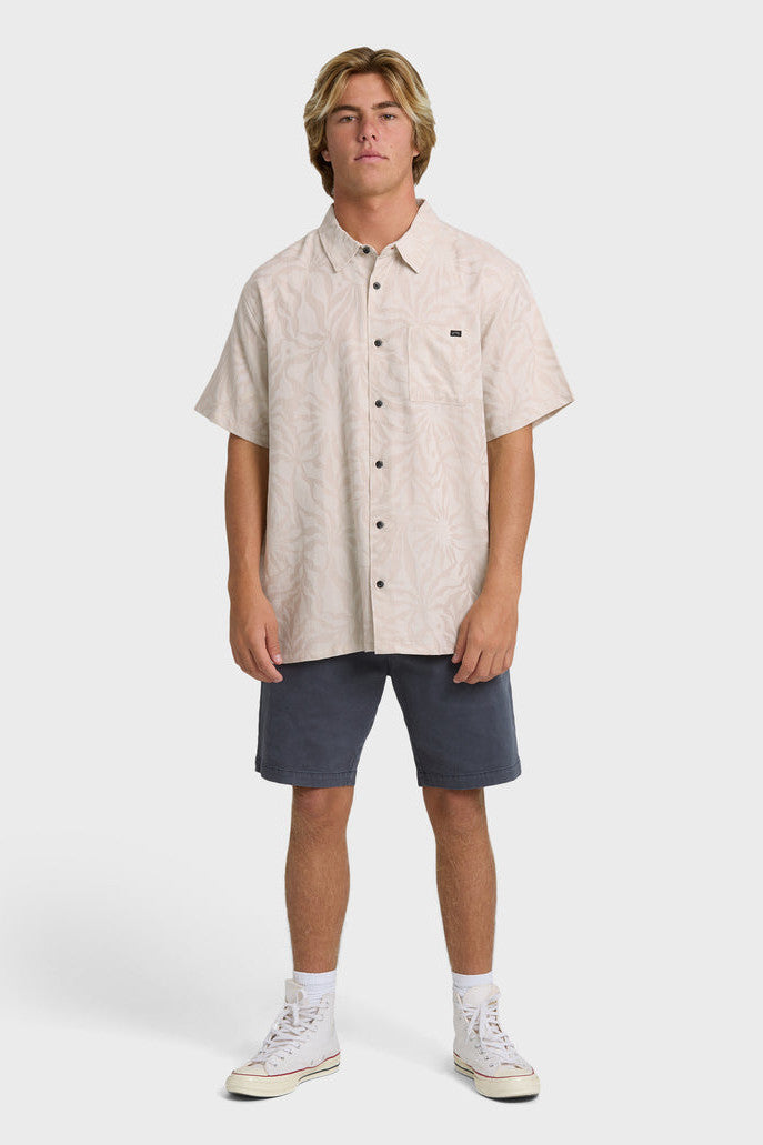 Man wearing a pink-grey short-sleeve button-up shirt with a tonal leaf pattern and navy shorts on a white background