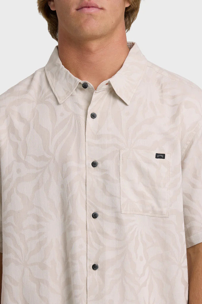 Man wearing a pink-grey short-sleeve button-up shirt with a tonal leaf pattern on a white background