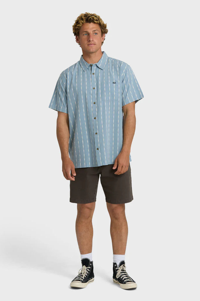 Man wearing a blue short-sleeve button-up shirt with a white stripe pattern with dark shorts on a white background