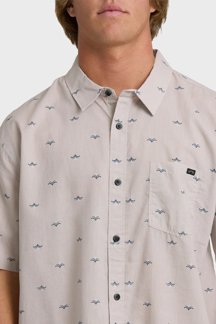 Detail shot of a man wearing a patterned light pink button-up collared shirt on a white background