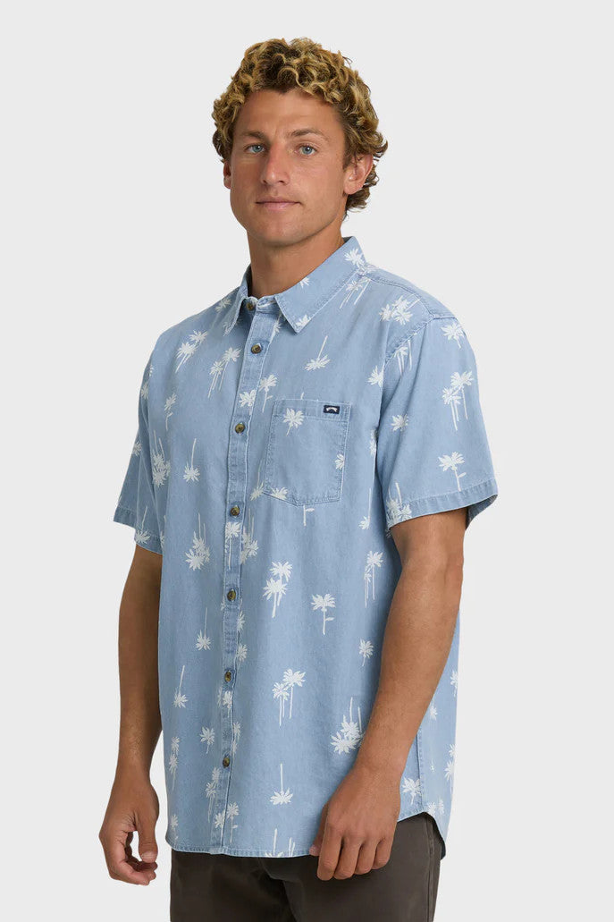 Man wearing a light blue button-up shirt with white palm tree pattern on a white background