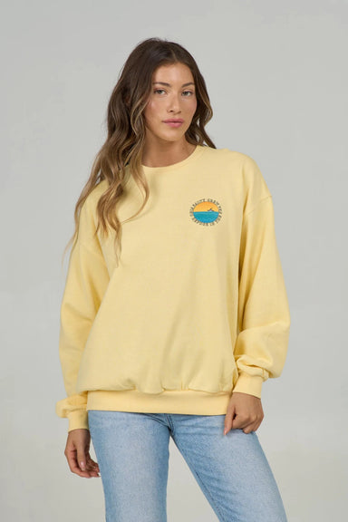 Woman wearing a yellow sweatshirt with a small chest graphic of a ship at sea on a gray background