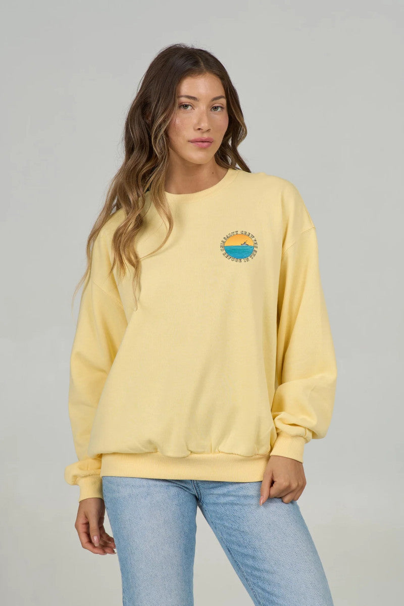 Woman wearing a yellow sweatshirt with a small chest graphic of a ship at sea on a gray background