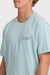 Person wearing a light blue t-shirt with a brand logo on a plain background
