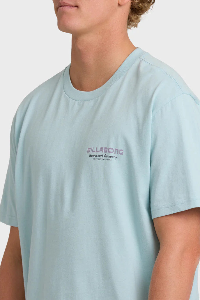Person wearing a light blue t-shirt with a brand logo on a plain background