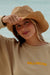 Woman wearing a straw hat and beige sweatshirt  against a light blue sky.