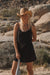 Woman in a black dress and straw hat standing in a desert landscape with rocks and sparse vegetation.