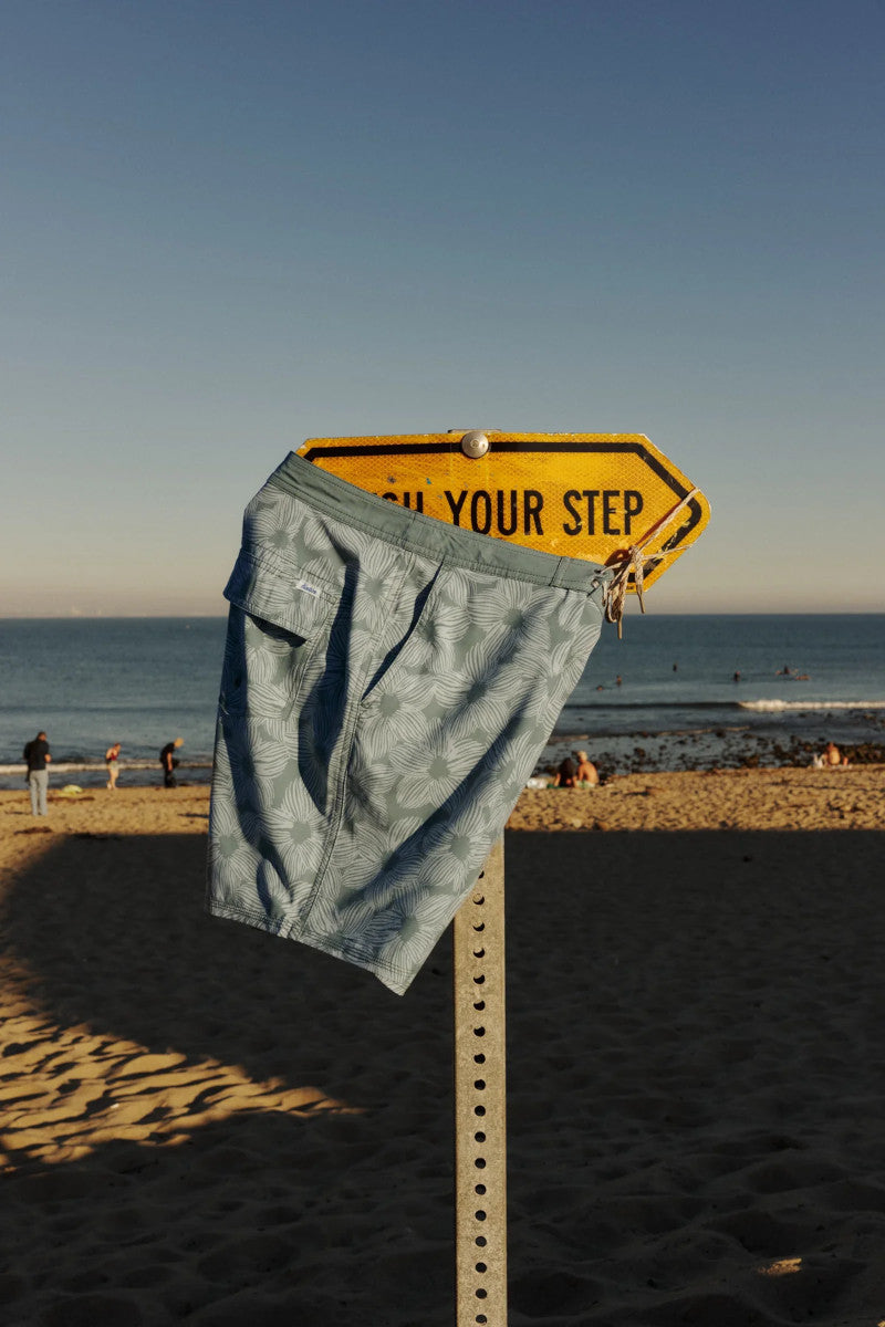 Blue floral shorts hanging on a yellow signpost at a beach.