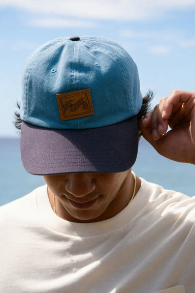 Man wearing a blue cap with a patch against a clear sky