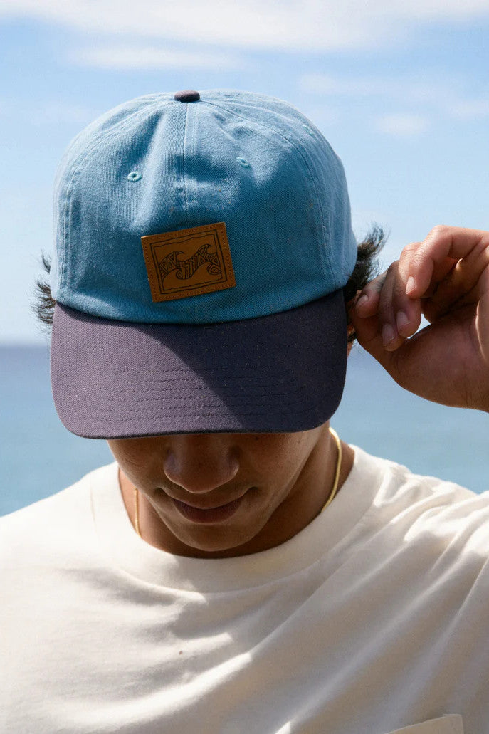 Man wearing a blue cap with a patch against a clear sky