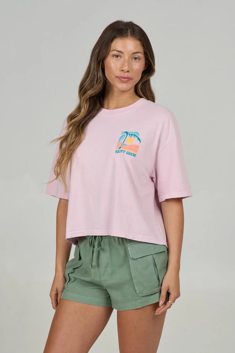 Woman wearing a pink t-shirt with a  palm tree chest graphic and green shorts on a plain background