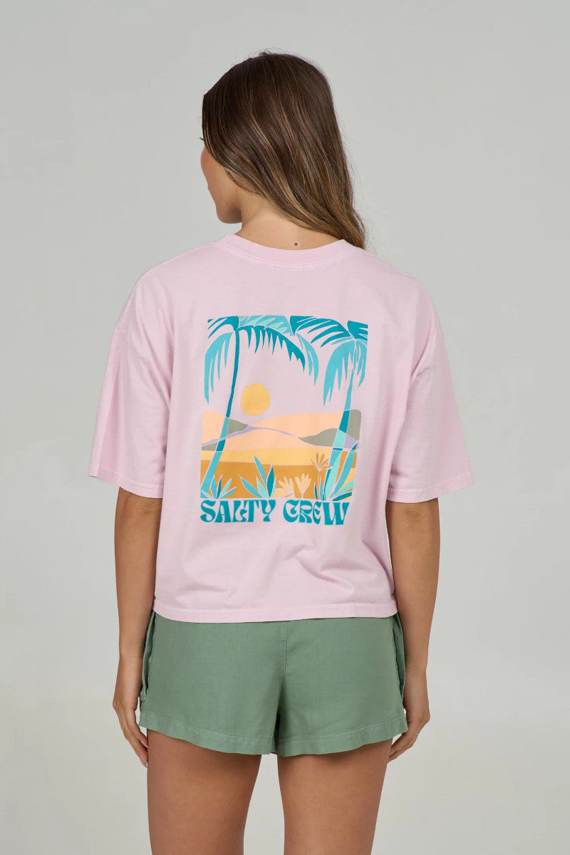 Back view of a woman wearing a pink t-shirt with a palm tree design and 'Salty Crew' text on a plain background