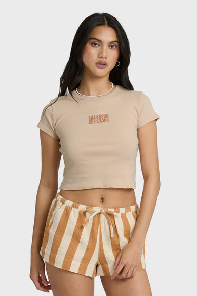 Woman wearing a beige crop top with Billabong text graphic and striped shorts on a white background