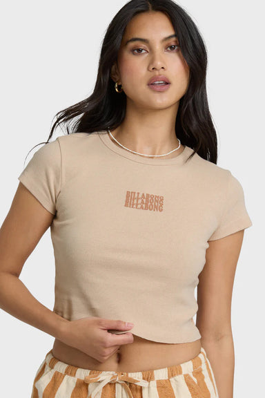 Woman wearing a beige crop top with Billabong text graphic and striped shorts on a white background