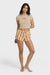 Woman wearing a beige crop top with Billabong text graphic and striped shorts on a white background