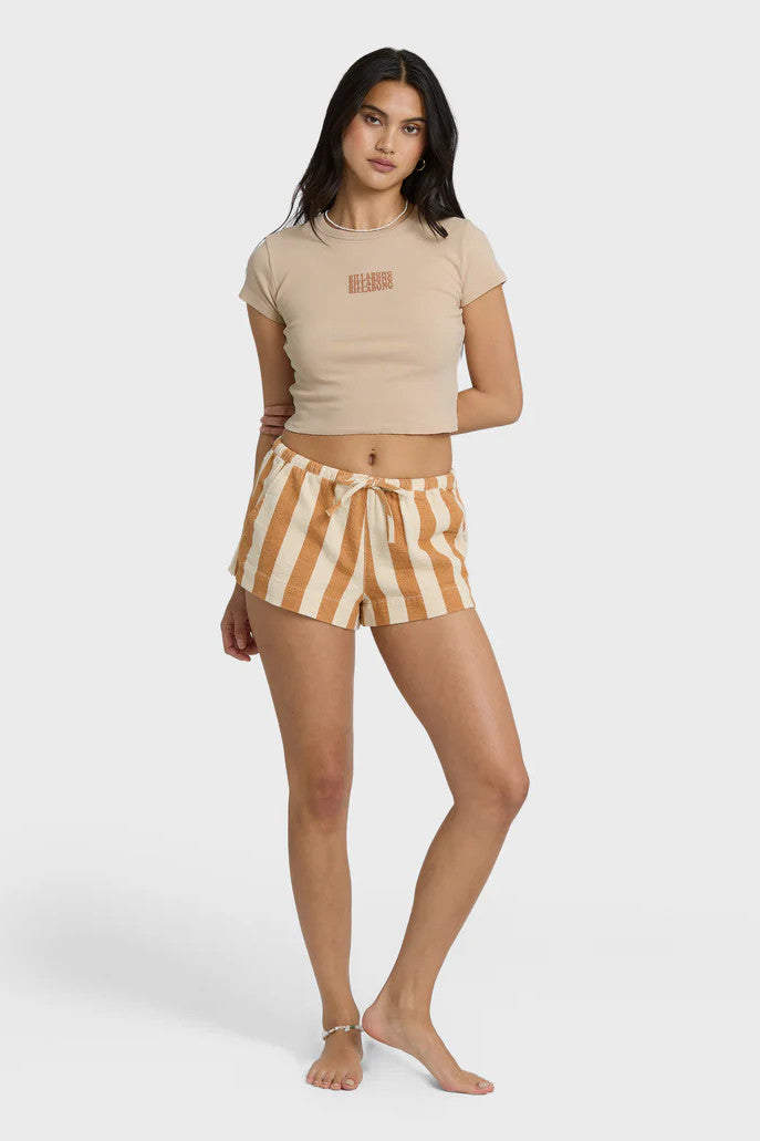 Woman wearing a beige crop top with Billabong text graphic and striped shorts on a white background