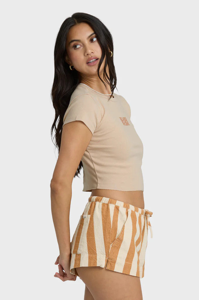 Woman wearing a beige crop top with Billabong text graphic and striped shorts on a white background