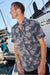 Man wearing a floral patterned shirt on a dock with boats in the background