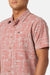 Man wearing a pink patterned shirt with a brand logo on a white background