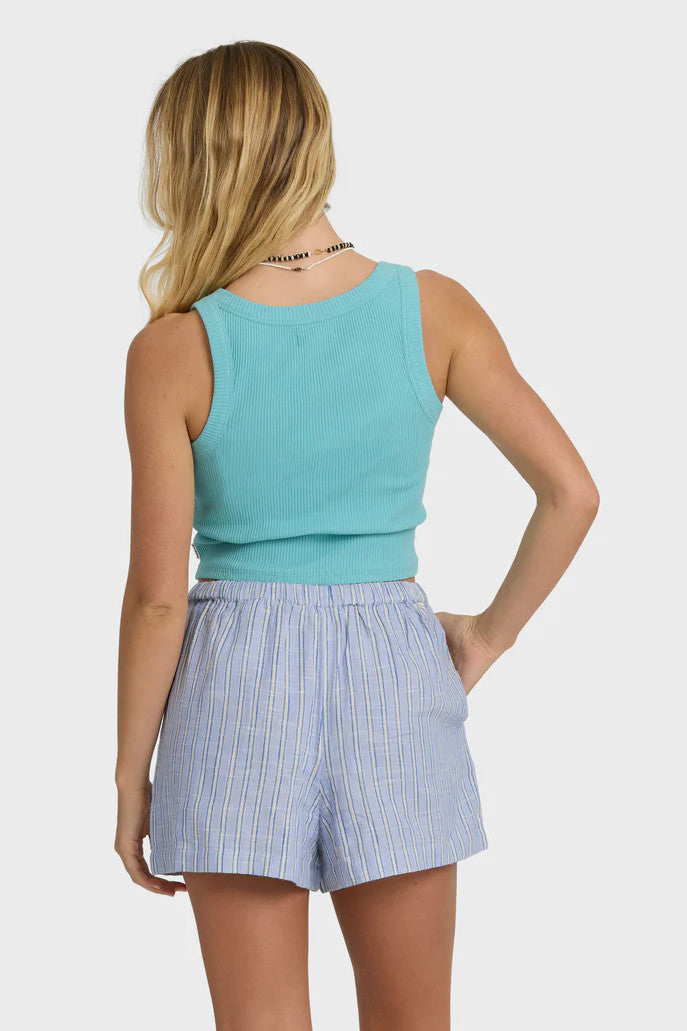 Back view of a woman wearing a turquoise tank top and blue plaid shorts on a white background