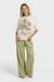 Woman wearing a cream t-shirt with a palm tree and surf shack graphic design and green striped pants on a white background