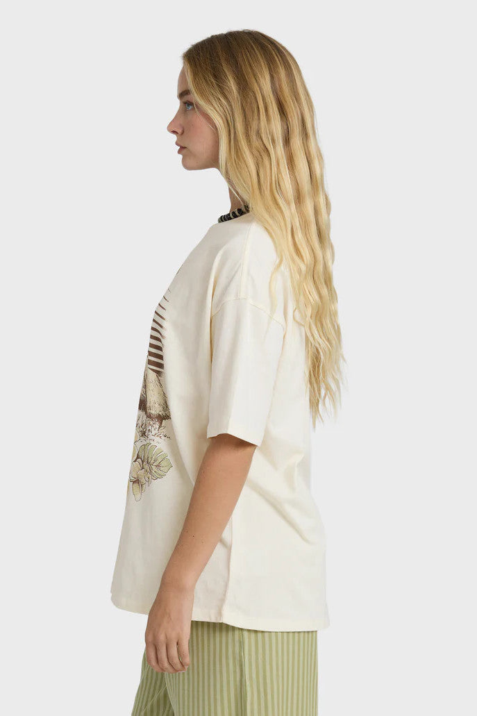 Woman wearing a cream t-shirt with a palm tree and surf shack graphic design and green striped pants on a white background