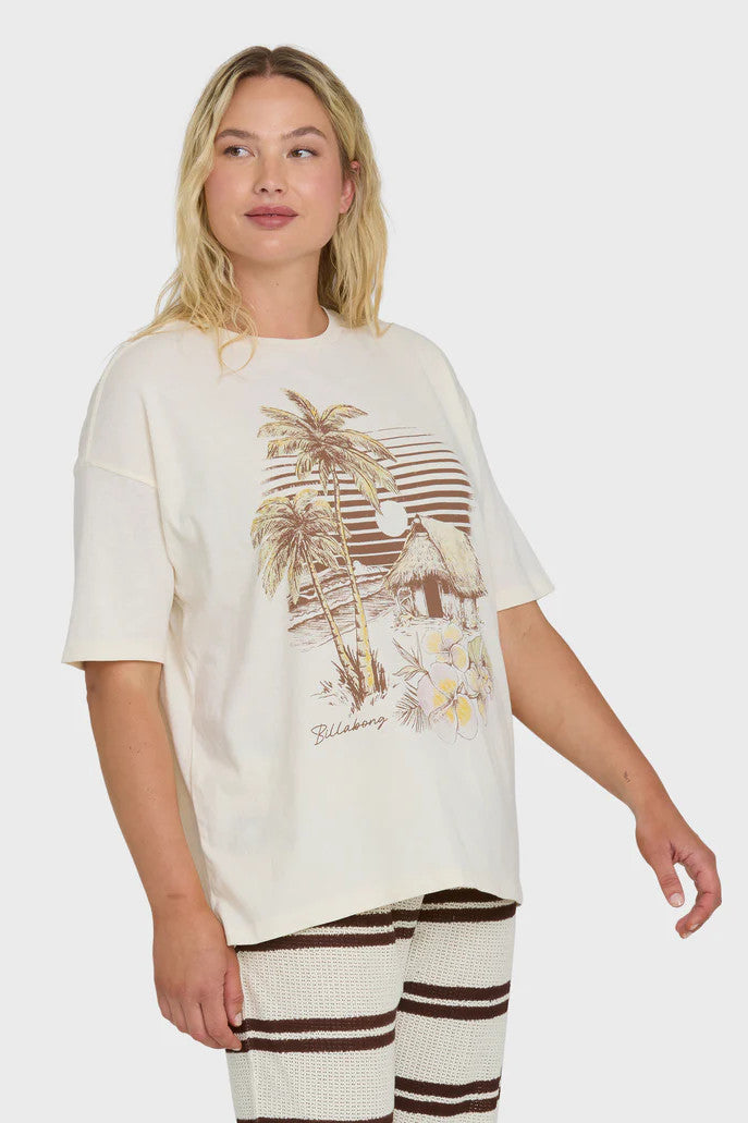 Woman wearing a cream t-shirt with a palm tree and surf shack graphic design and striped pants on a white background